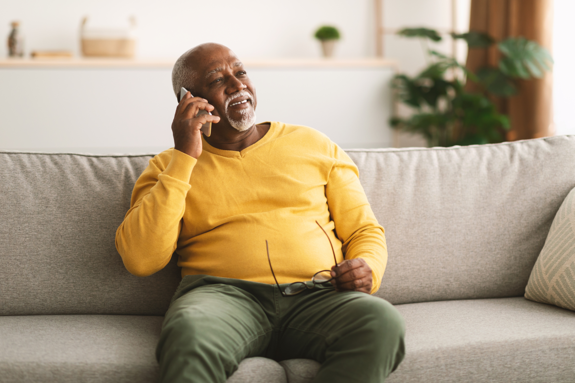 Man in yellow top on the phone on the sofa smiling